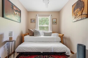 A bedroom with a bed, a window with blinds, a small table with a lamp, and artwork on the walls. - The Endless Summer-hot Tub-7 Beds (North Charleston)