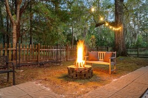 A wooden bench with a fire pit in the center, surrounded by a wooden fence and trees. - The Endless Summer-hot Tub-7 Beds (North Charleston)