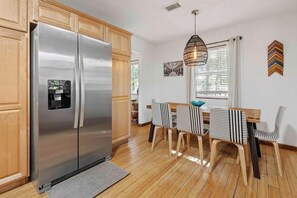 A kitchen with a stainless steel refrigerator, wooden cabinets, a dining table with striped chairs, and a hanging light fixture. - The Endless Summer-hot Tub-7 Beds (North Charleston)