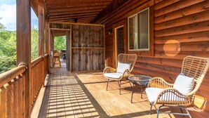 A wooden cabin with a porch, wicker chairs, and a view of the outdoors. - Majestic Lodge | Theater & Game Rm, Hocking Hills (Creola)