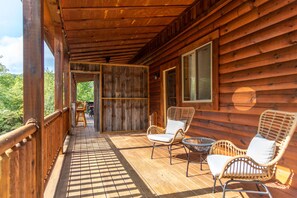 A wooden cabin with a porch, wicker chairs, and a view of the outdoors. - Majestic Lodge | Theater & Game Rm, Hocking Hills (Creola)