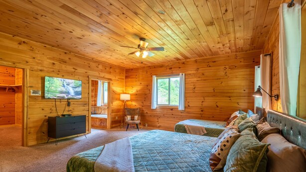 A log cabin bedroom with a bed, two bedside tables, a chair, a TV, and a ceiling fan. - Majestic Lodge | Theater & Game Rm, Hocking Hills (Creola)