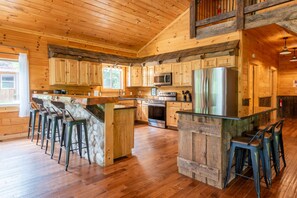 A spacious kitchen with wooden cabinets, a large island with stools, stainless steel appliances, and a stone accent wall. - Majestic Lodge | Theater & Game Rm, Hocking Hills (Creola)