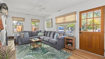 A living room with a grey sectional sofa, a coffee table, a wooden side table, and a large window with a view of the outdoors.
