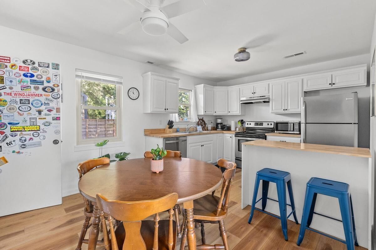Una cocina moderna con armarios blancos, un refrigerador de acero inoxidable y una mesa de comedor de madera con sillas.