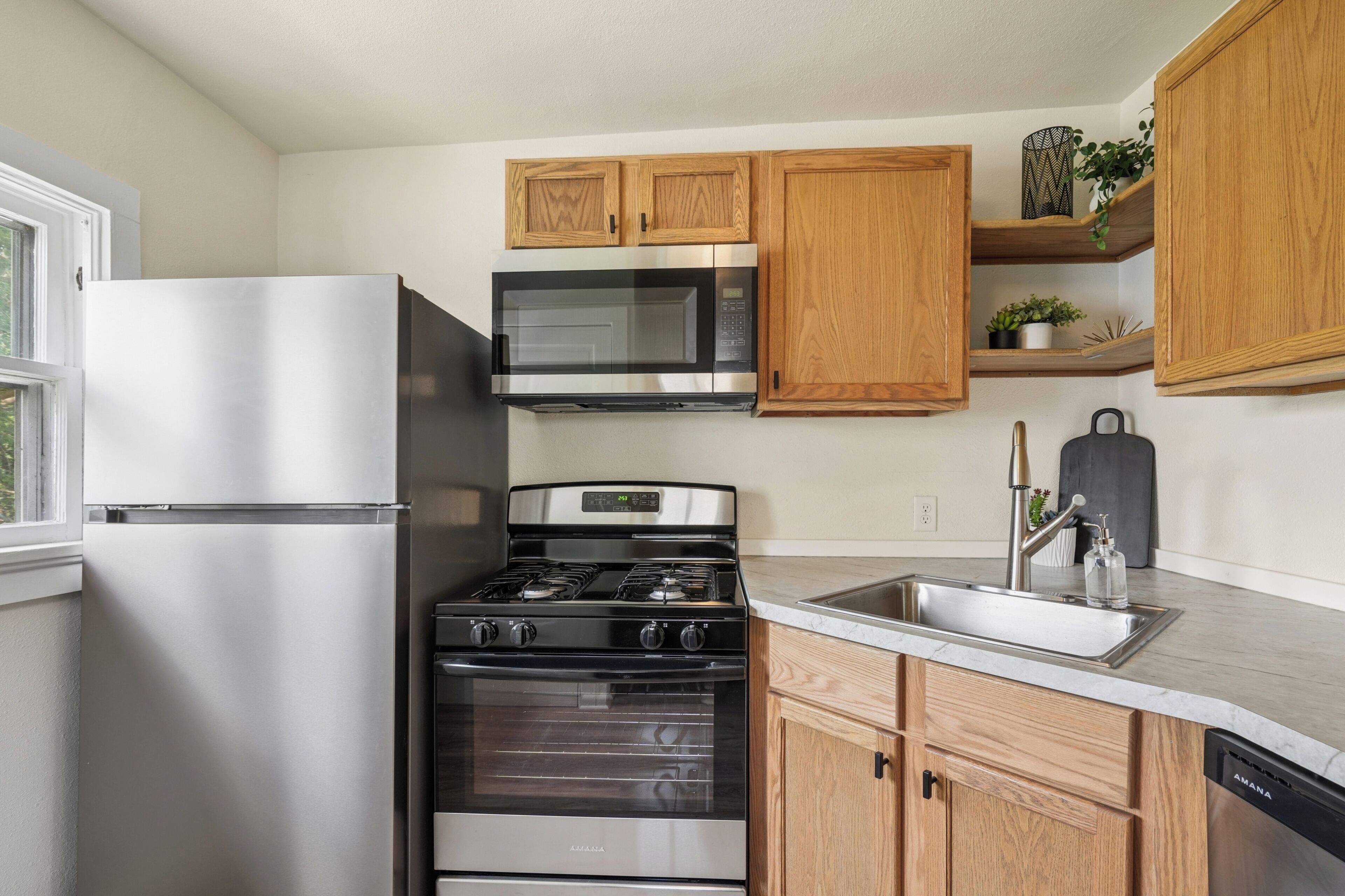 Una cocina con refrigerador de acero inoxidable, microondas, estufa y armarios de madera.