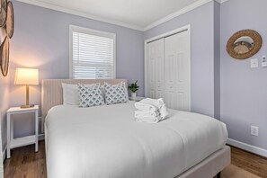 Una cama bien hecha con sábanas blancas, una lámpara de noche y una ventana con persianas.
