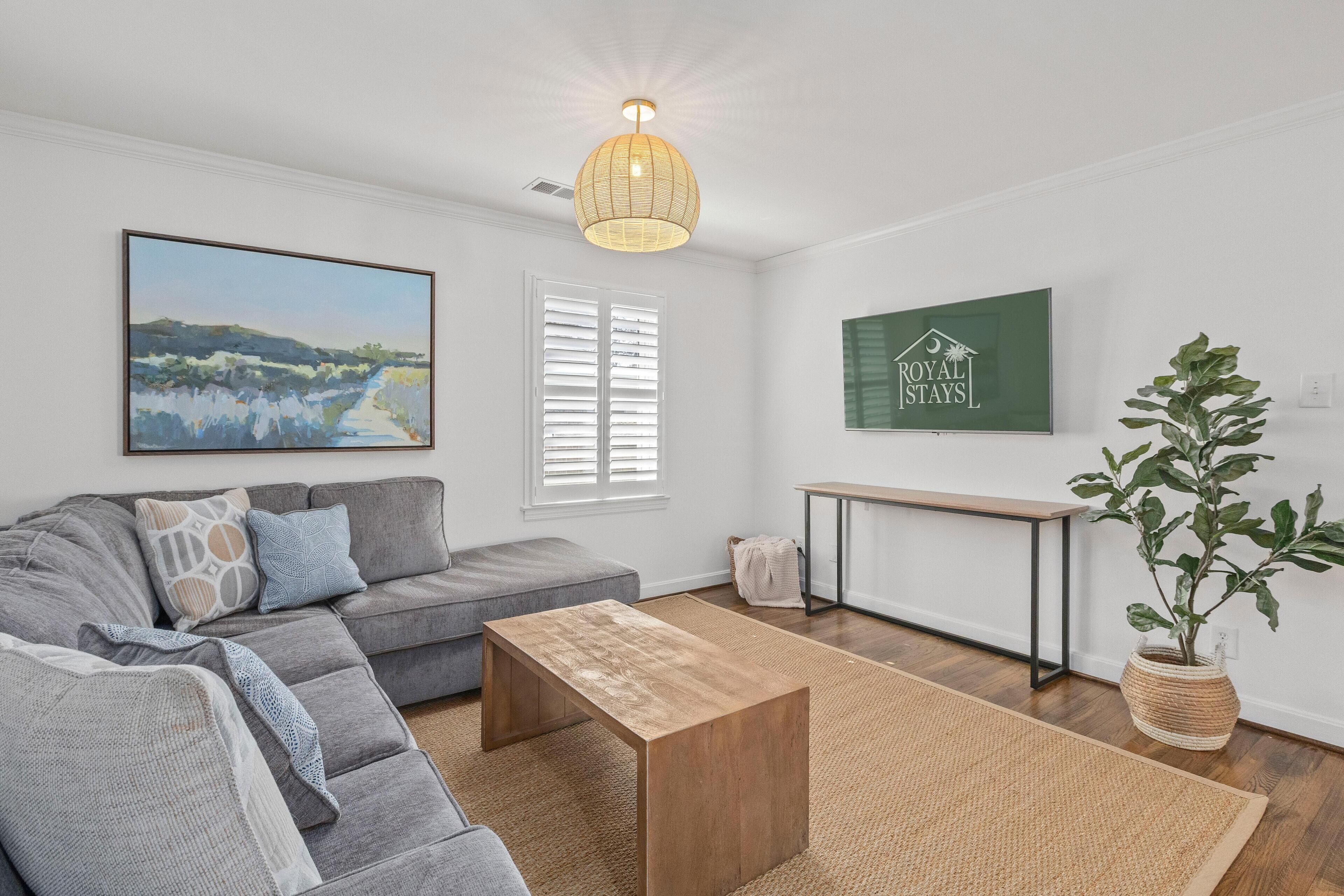 Un salon moderne avec un canapé gris, une table basse en bois, un tableau, un panneau vert et une plante en pot.