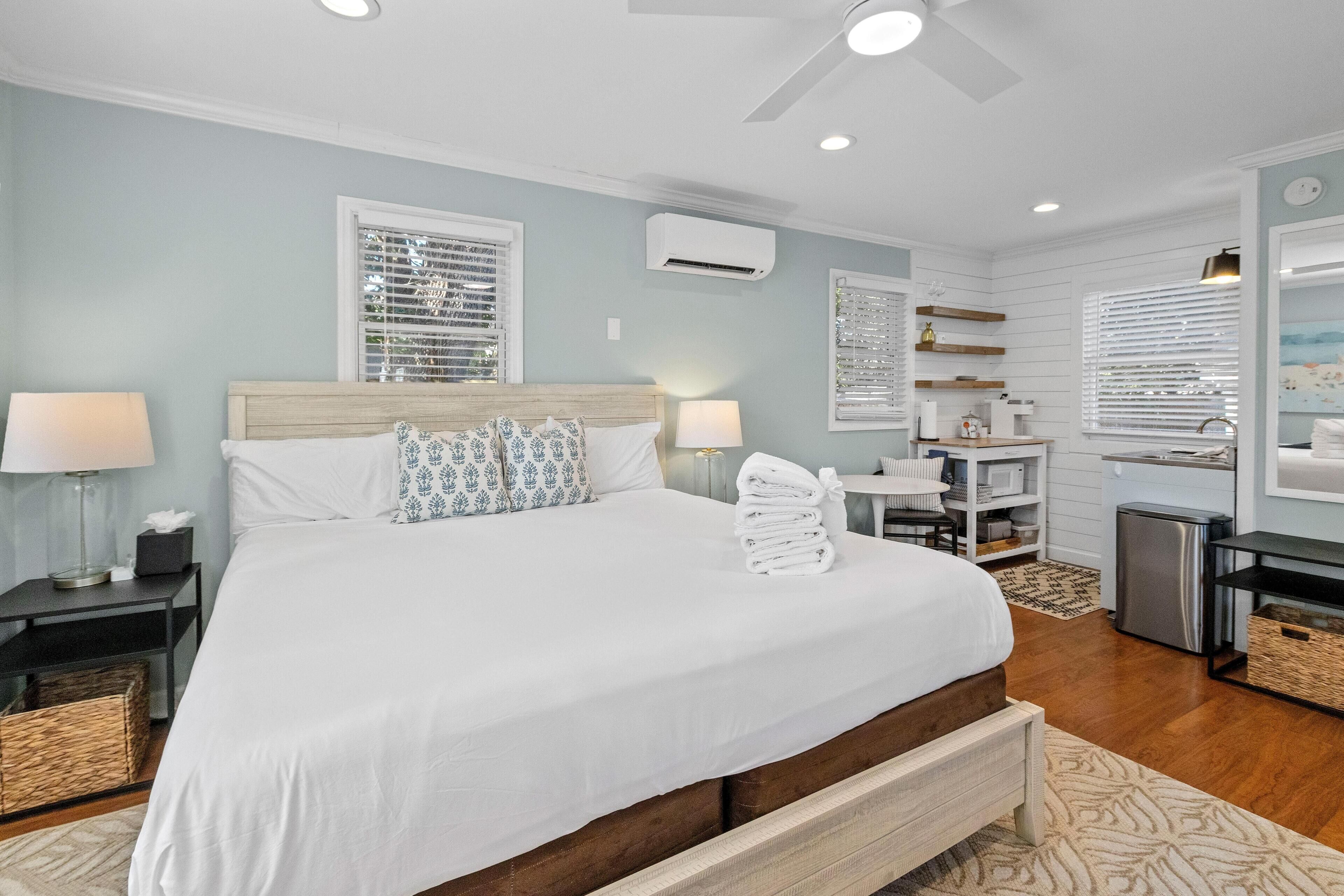 A modern hotel room with a large bed, bedside tables, a desk, and a kitchenette.