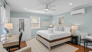 A bedroom with a bed, bedside tables, a desk with a chair, a vanity with a mirror, and a ceiling fan. - Old Village Palmetto- Pet Friendly (Mount Pleasant)