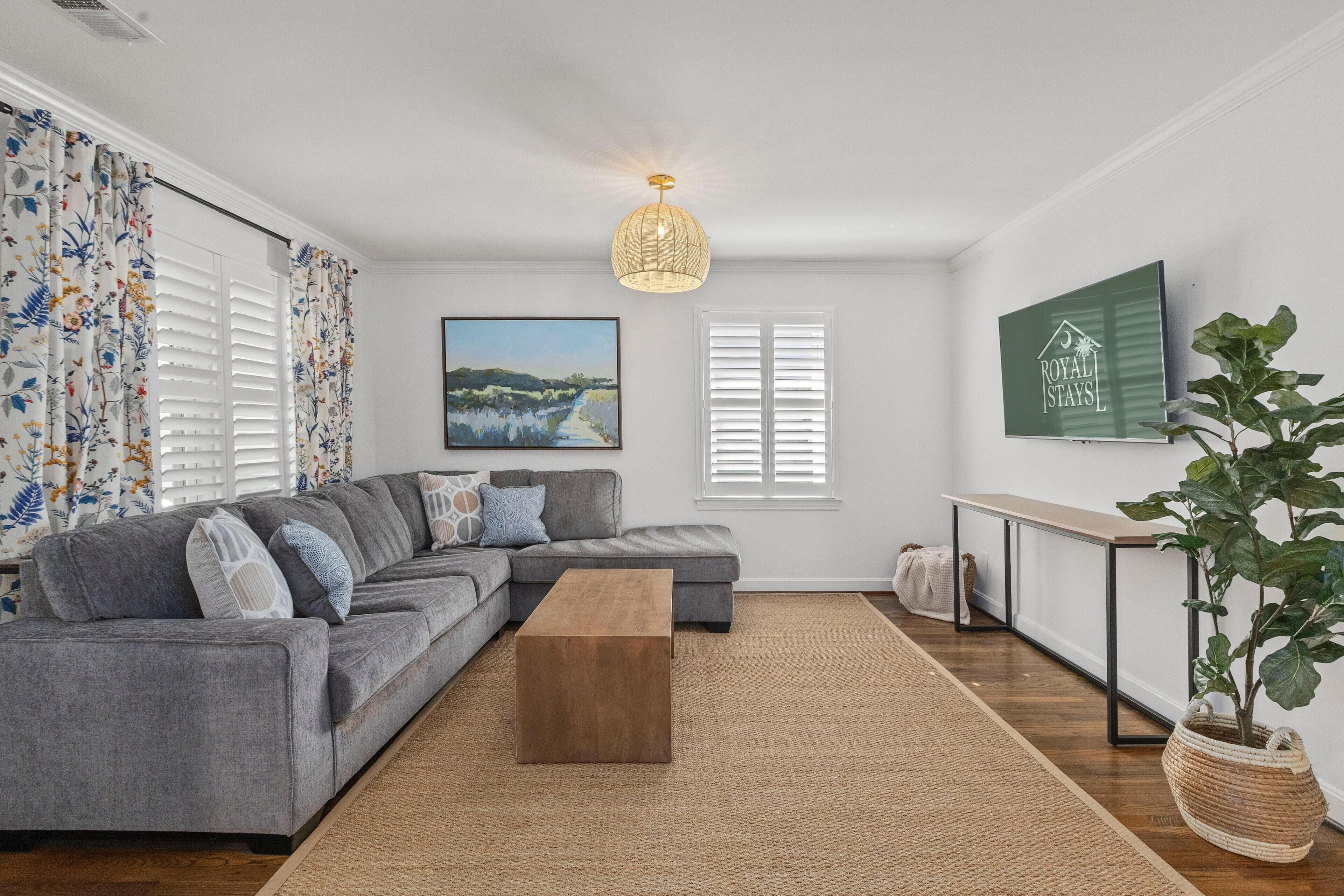 Ein modernes Wohnzimmer mit einem grauen Ecksofa, einem Holztisch, einer Pendelleuchte und einem gerahmten Bild an der Wand.