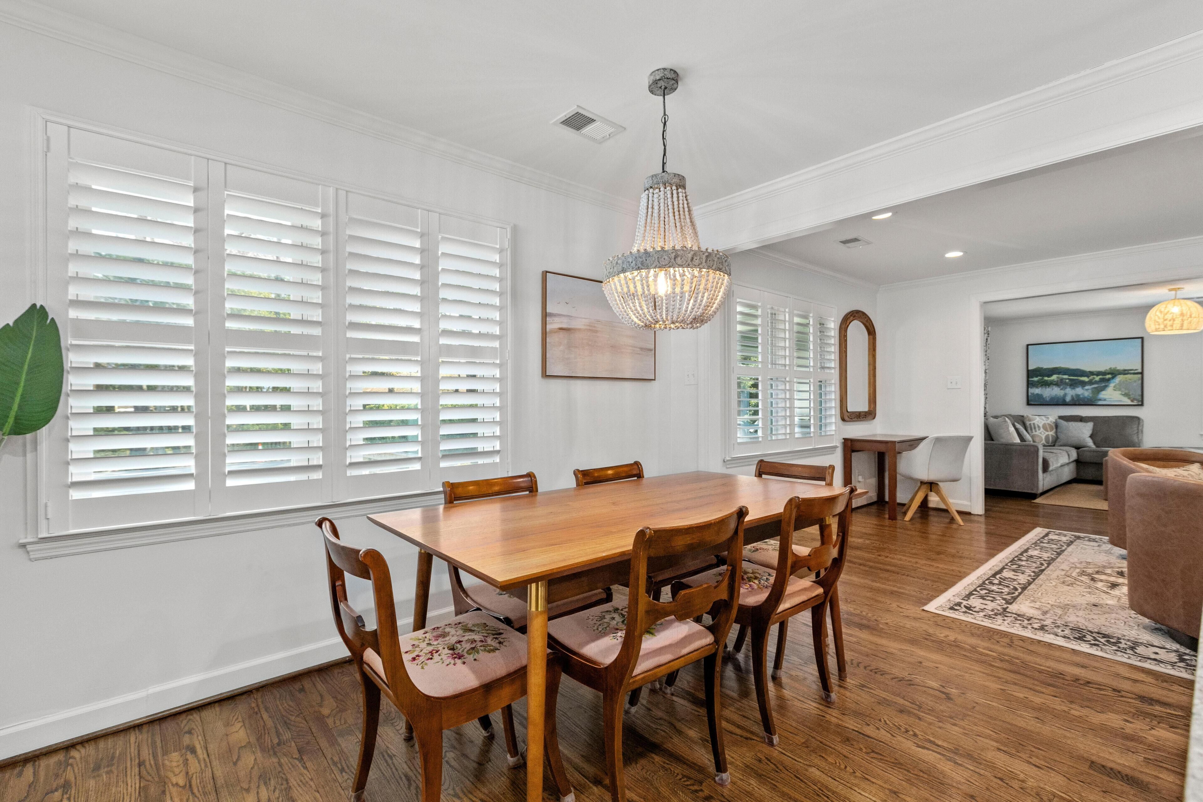 A dining area with a wooden table and chairs, white walls, and a chandelier.
