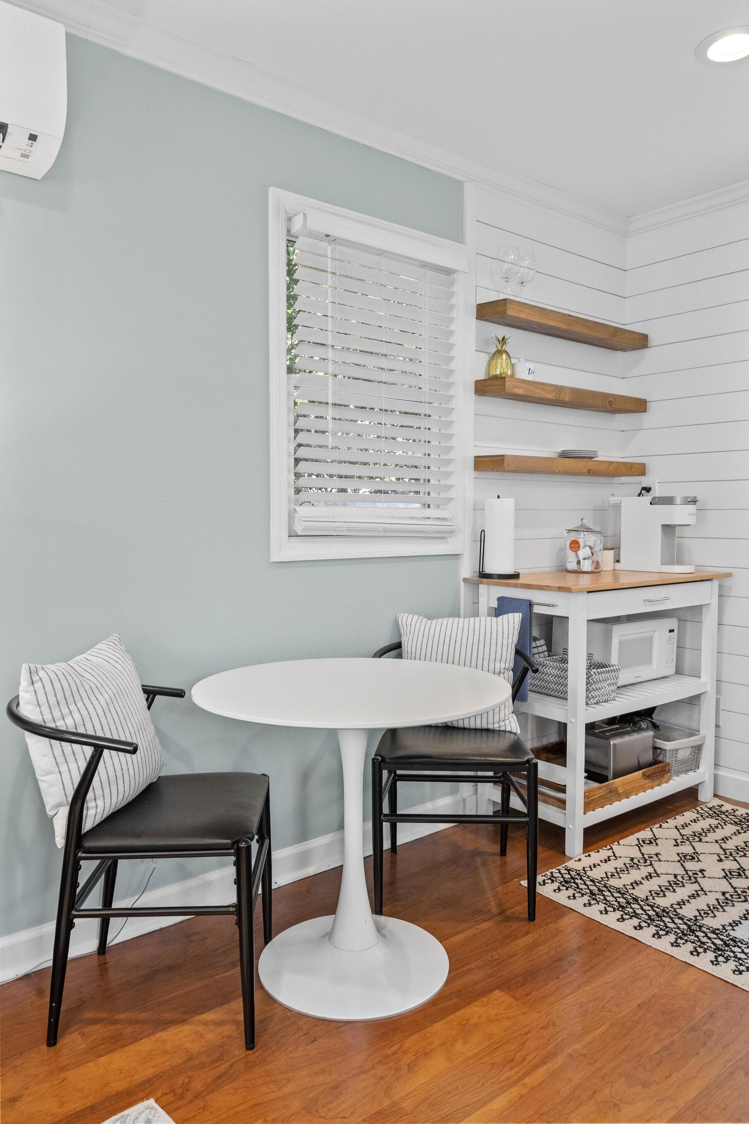 Une cuisine de taille réduite avec des meubles blancs, une table à manger blanche et une chaise noire.