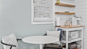 Une cuisine de taille réduite avec des meubles blancs, une table à manger blanche et une chaise noire.