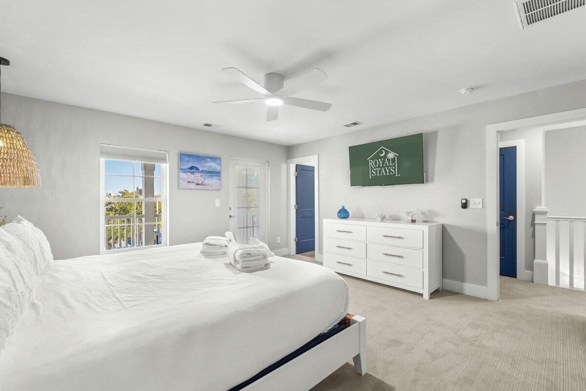 A modern bedroom with a large bed, a ceiling fan, a dresser, and a view of the outdoors.