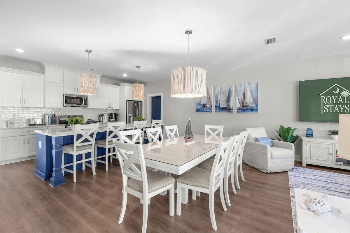 A modern kitchen with white cabinets, a central island, and a dining area with white chairs.