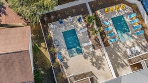 Vue aérienne d’une cour arrière avec deux piscines, entourée de chaises longues et de parasols.