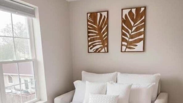 Une chambre à coucher avec un lit, du linge de lit blanc, une fenêtre et deux œuvres d’art murales.
