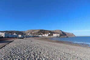 A pebble beach with a promenade, buildings, and a hill in the background. - Mona Lodge (Llandudno)