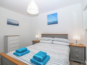 A bedroom with a bed, two bedside tables, a nightstand, a dresser, and two wall-mounted pictures. - Mona Lodge (Llandudno)