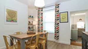 Zona pranzo con tavolo e sedie in legno, lampada a sospensione, libreria e finestra con tenda decorata.