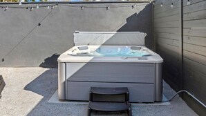 Ein Whirlpool mit Sitzbank davor, umgeben von einem dunklen Zaun und einem klaren Himmel.