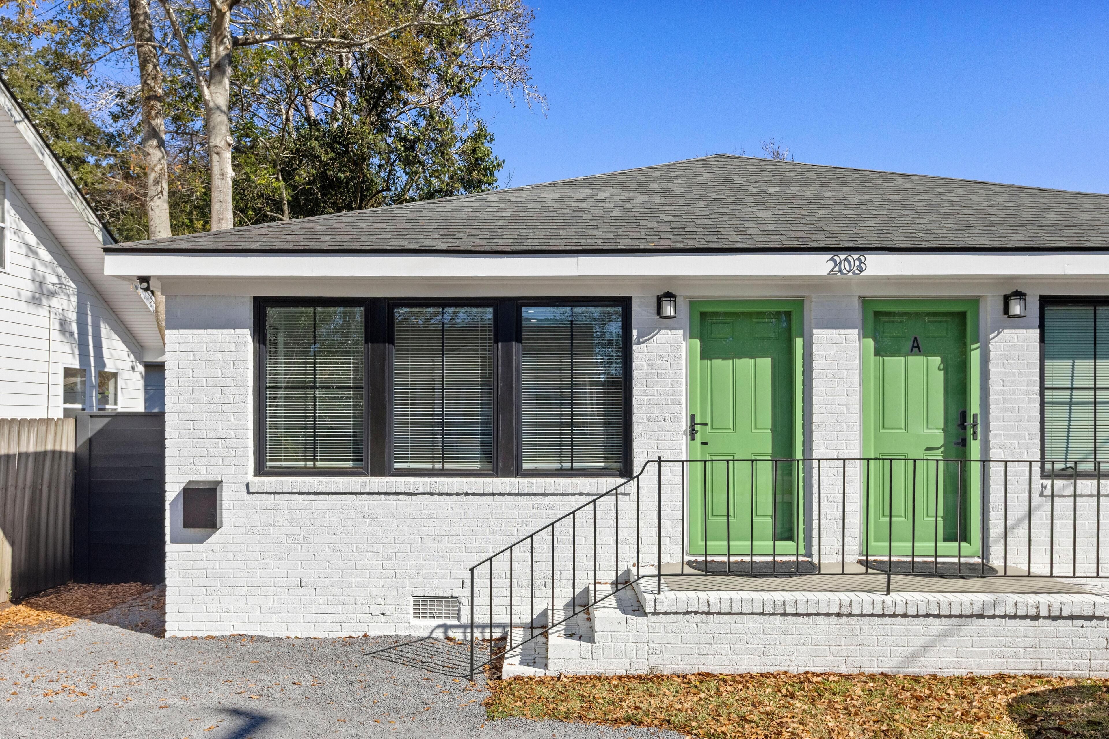 A single-story house with white brick exterior, two green doors, and a number '203' on the front.