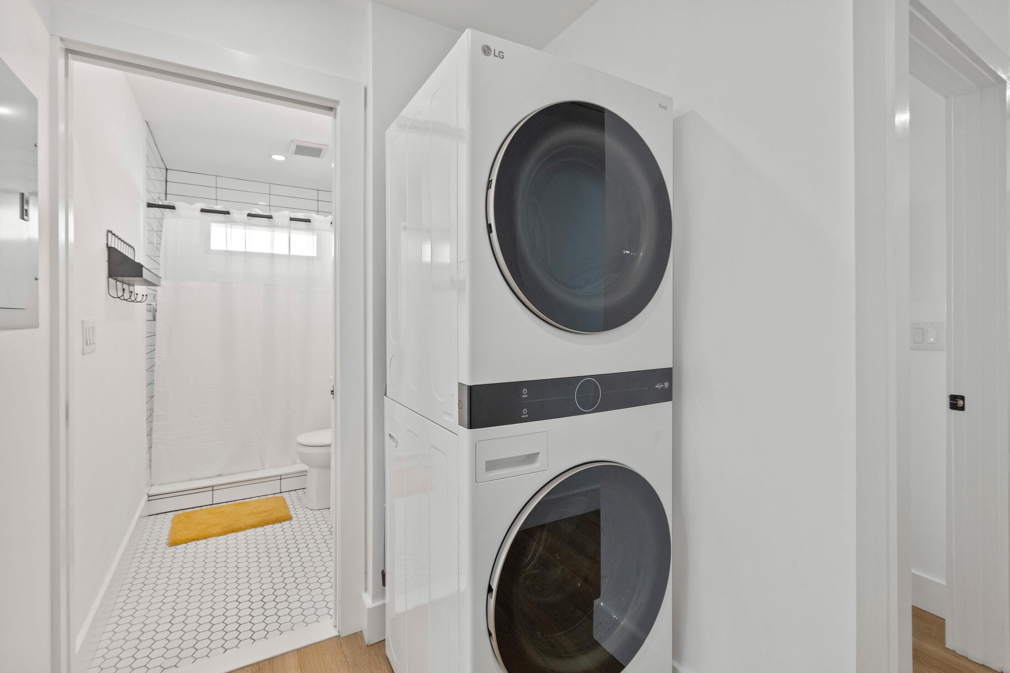 A modern laundry room with two stacked washing machines, a shower area, and a yellow mat on the floor.