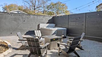 Een terras buiten met een jacuzzi, zithoek en sfeerverlichting.