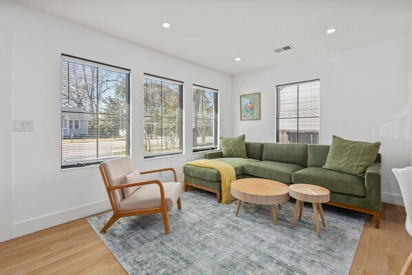 A modern living room with a green sofa, a wooden chair, and two round wooden tables.