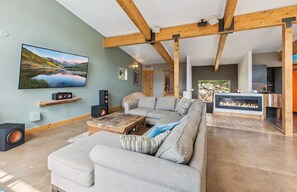 A living room with a sectional sofa, a flat-screen TV, wooden beams, a fireplace, and a kitchen area. - Stellar Peak Chalet, Home in the Colorado Mountains (Montezuma)