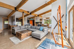 Ein geräumiger Wohnbereich mit Ecksofa, Holzbalken, einem Couchtisch und einer Schaukel.