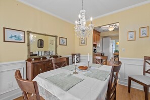Ein Esszimmer mit einer Chandelüster, Holzmöbeln und gerahmten Kunstwerken an den Wänden.