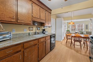 A kitchen with wooden cabinets, a dishwasher, and a toaster. There is a dining area with a table and chairs. - The Victorian Jewel Pet Friendly (Mount Pleasant)