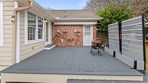 Une terrasse couverte avec un mur en briques, une porte blanche et une petite table entourée de chaises.