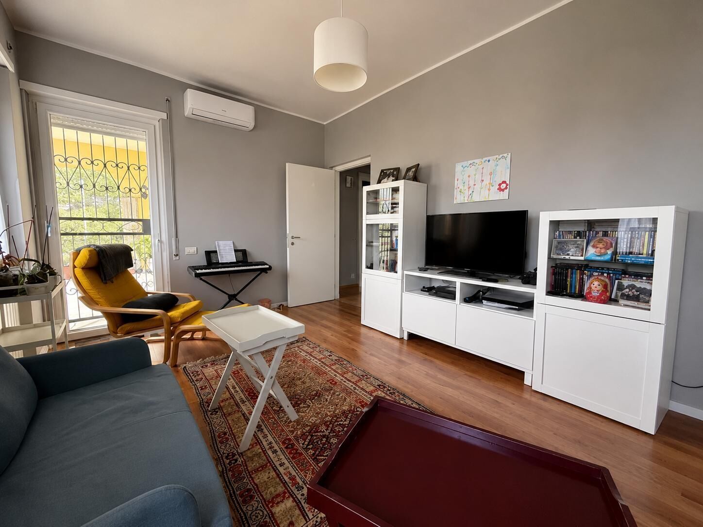 A living room with a sofa, a television, a bookshelf, a piano, and a dining table.