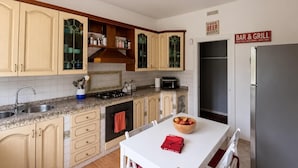 A kitchen with wooden cabinets, a stove, a sink, and a refrigerator. There is a table with a bowl of fruit and a red napkin.