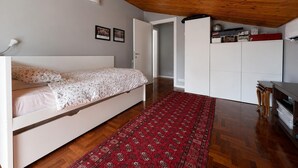 A bedroom with a bed, a red patterned rug, a white wardrobe, and a wooden ceiling.