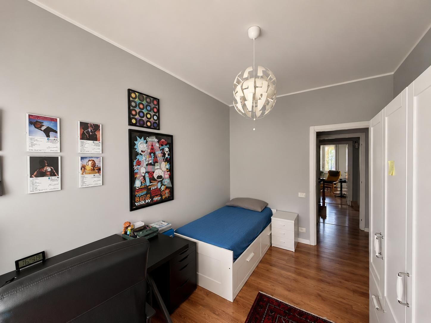 A bedroom with a bed, a desk, a chair, and a wall clock.