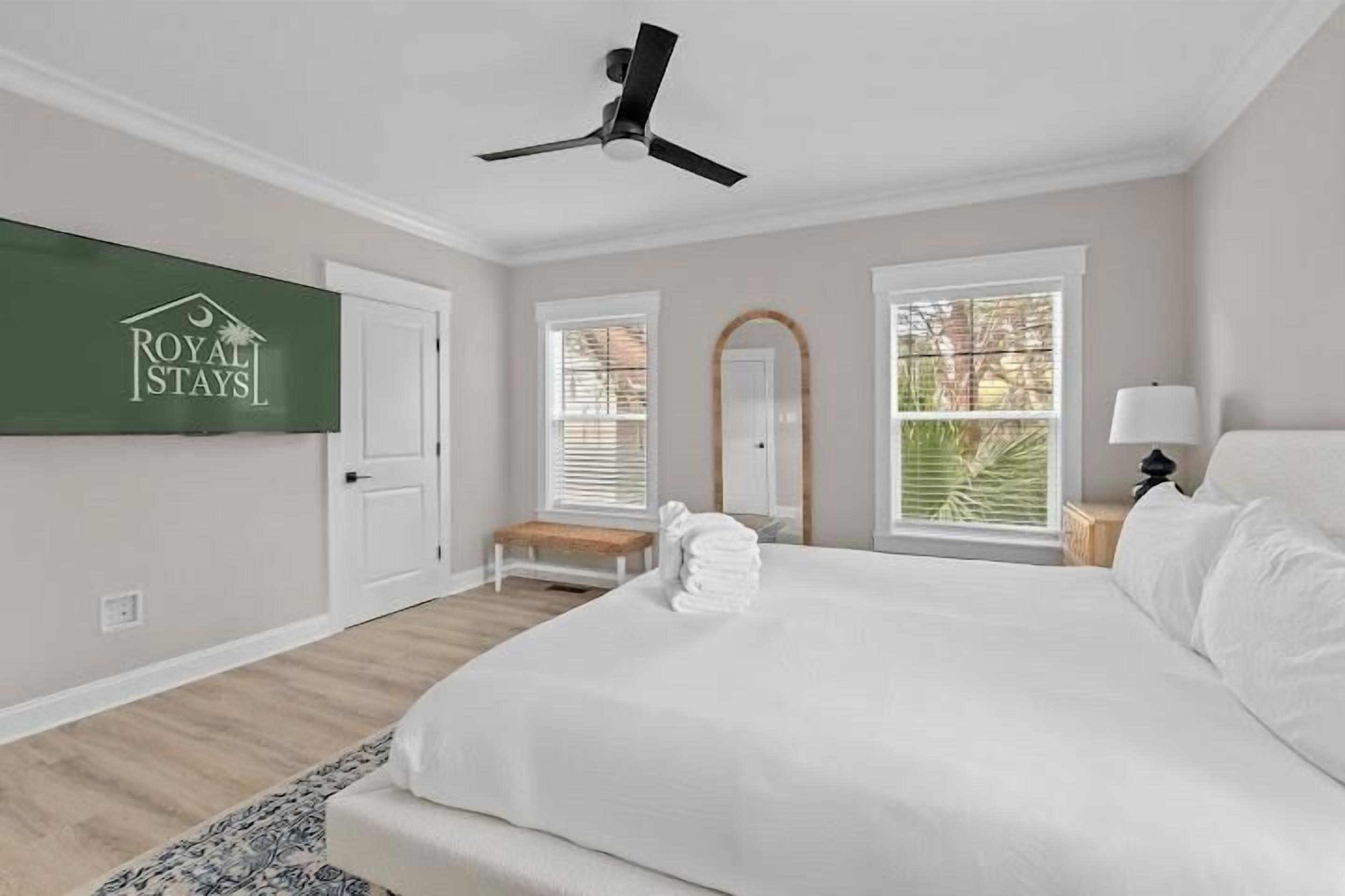 Une chambre d’hôtel avec un lit, un ventilateur de plafond, un banc, un miroir et une fenêtre avec des stores.