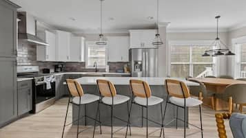 A modern kitchen with white cabinets, a central island with bar stools, stainless steel appliances, and pendant lighting.