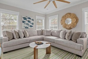 A modern living room with a light gray sectional sofa, a round coffee table, and a large decorative mirror on the wall. - Beach Belle- Pet Friendly- Luxury Edisto Home (Edisto Island)
