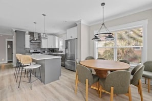 Een moderne keuken met een centraal eiland, barstoelen en een eettafel met stoelen.