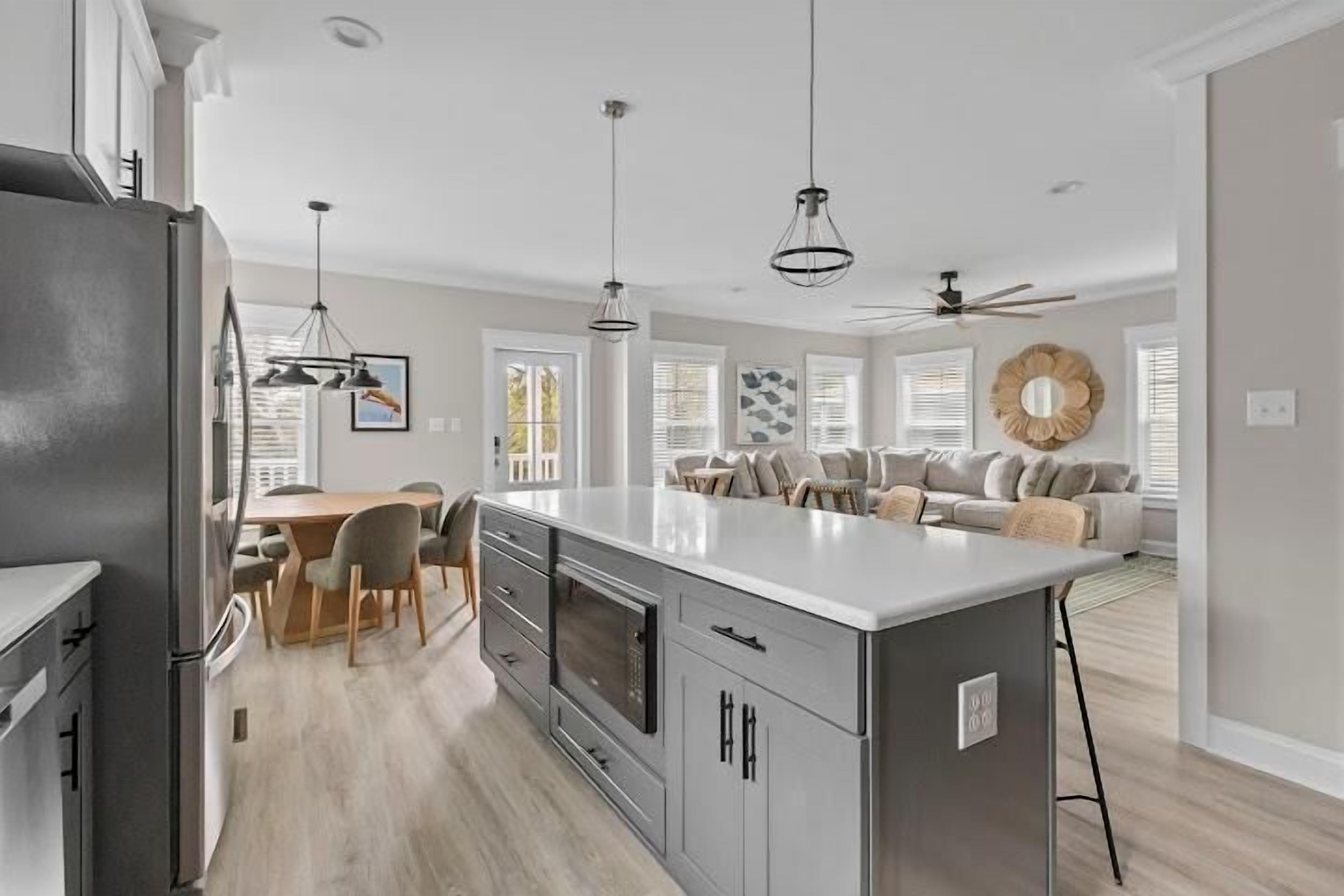 A modern kitchen with grey cabinetry, a central island, and a dining area with a wooden table and chairs.