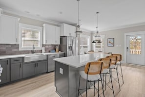 Een moderne keuken met grijze kasten, een groot eiland met barkrukken en hanglampen.