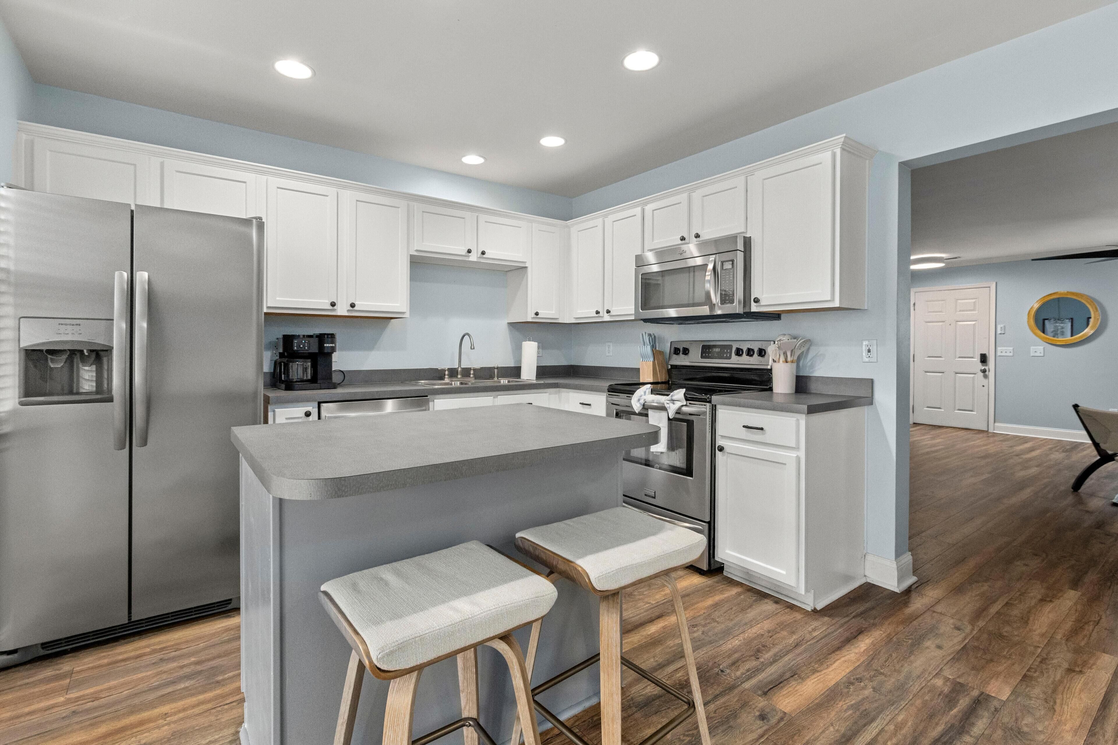 A modern kitchen with white cabinets, stainless steel appliances, and a central island with bar stools.