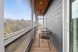 A covered balcony with a ceiling fan, wooden floor, and two chairs. - Wild Tide-pool-pet Friendly (Edisto Island)
