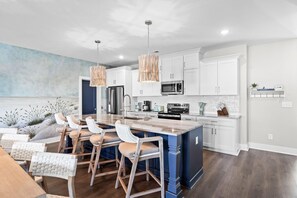 A modern kitchen with white cabinets, a central island, bar stools, and pendant lighting. - Between Tides-pool- Walk to Beach (Murrells Inlet)