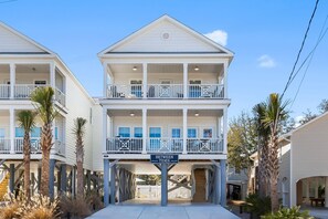 Un edificio de dos pisos frente a la playa con balcones, un letrero que dice "BETWEEN TIDES" y palmeras.