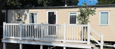 A mobile home with a white deck, a small porch, and a chimney.